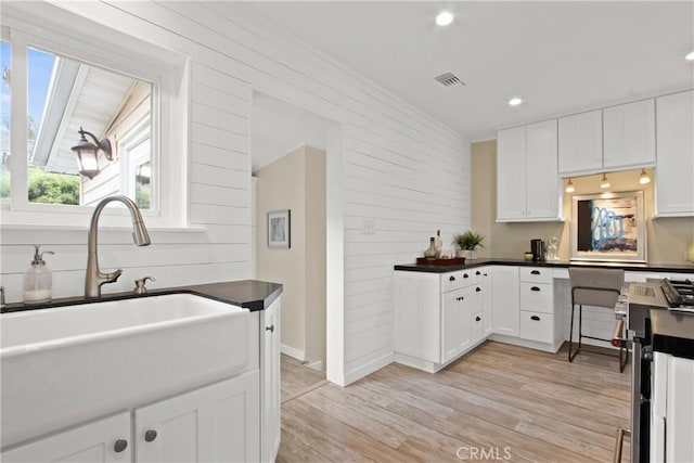 4841 E Los Coyotes Diagonal, Long Beach, CA 90815 - kitchen featuring dark countertops, light wood-type flooring, white cabinets, wooden walls, and recessed lighting
