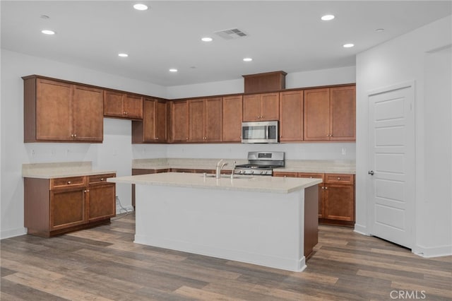 1649 Spring Run Ln, Beaumont, CA 92223 - kitchen with appliances with stainless steel finishes, dark wood-style flooring, light countertops, brown cabinetry, and an island with sink