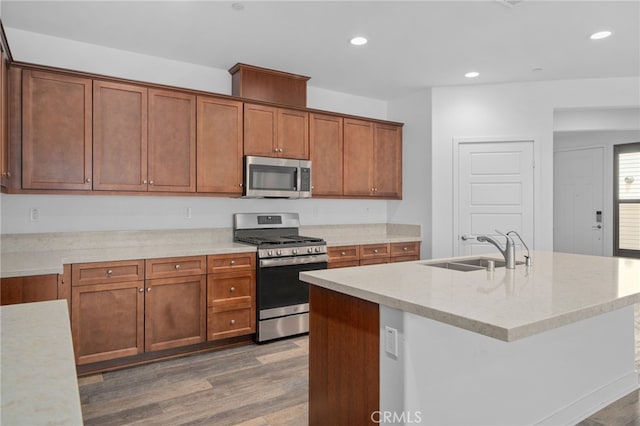 1649 Spring Run Ln, Beaumont, CA 92223 - kitchen featuring appliances with stainless steel finishes, wood finished floors, recessed lighting, brown cabinetry, and a kitchen island with sink