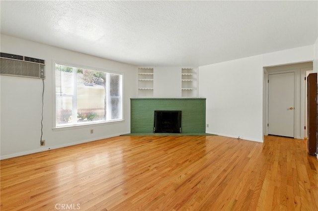 2723 57th St, Sacramento, CA 95817 - unfurnished living room with light wood-style flooring, built in features, a fireplace, an AC wall unit, and a textured ceiling