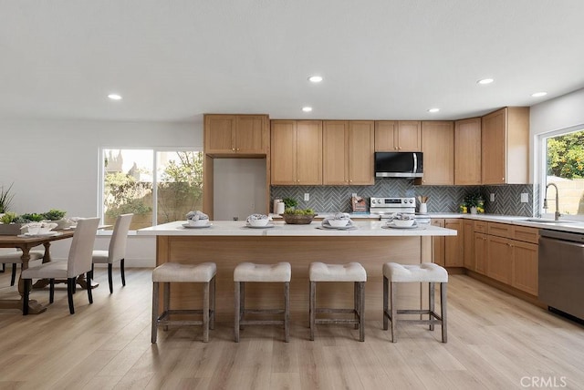 13020 Beach St, Cerritos, CA 90703 - kitchen featuring appliances with stainless steel finishes, decorative backsplash, light countertops, light wood-type flooring, and a center island