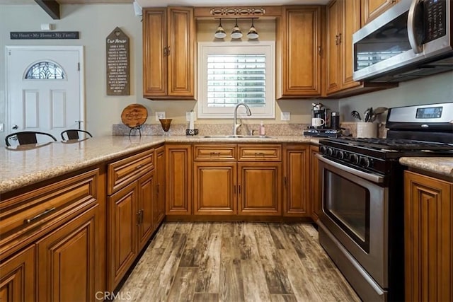 182 Darfo Dr, Crestline, CA 92325 - kitchen with stainless steel appliances, brown cabinets, light wood finished floors, a peninsula, and light stone countertops