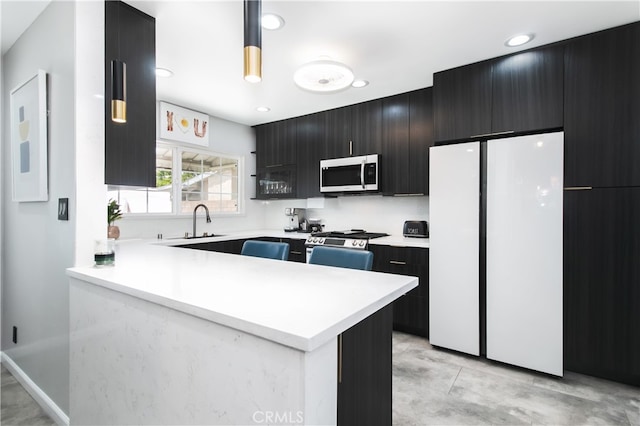 8527 Casaba Ave, Winnetka, CA 91306 - kitchen featuring stainless steel appliances, dark cabinets, light countertops, hanging light fixtures, and a peninsula
