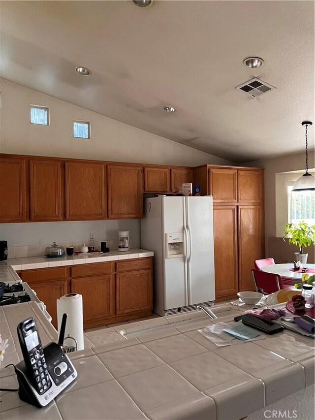 14106 Dartmouth St, Hesperia, CA 92344 - kitchen featuring white fridge with ice dispenser, tile counters, brown cabinetry, vaulted ceiling, and hanging light fixtures