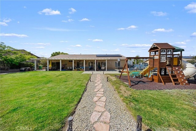 1410 Charles St, Banning, CA 92220 - rear view of house with a lawn, a patio area, roof mounted solar panels, and a playground