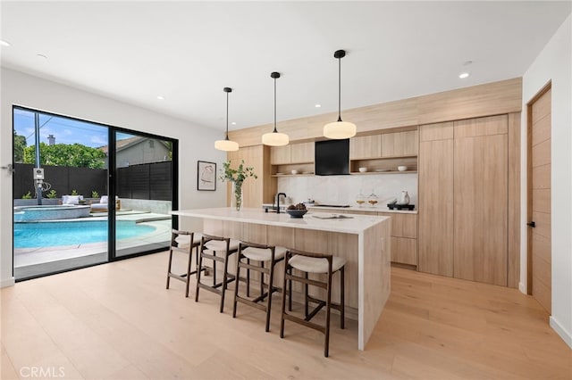 555 N Plymouth Blvd, Hancock Park, CA 90004 - kitchen featuring light brown cabinetry, modern cabinets, light wood finished floors, a kitchen bar, and tasteful backsplash