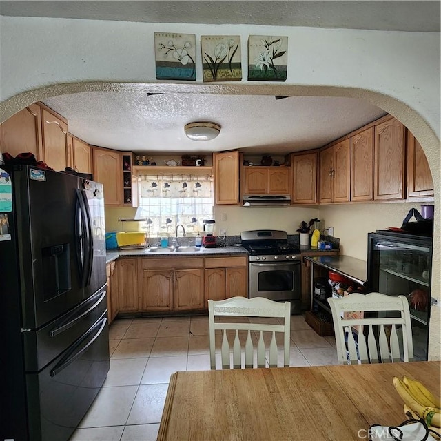3322 E 8th St, Los Angeles, CA 90023 - kitchen with black refrigerator with ice dispenser, stainless steel gas range, arched walkways, under cabinet range hood, and light tile patterned floors