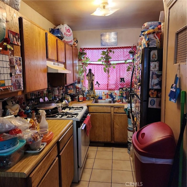 3322 E 8th St, Los Angeles, CA 90023 - kitchen featuring under cabinet range hood, gas range gas stove, light tile patterned floors, and brown cabinets