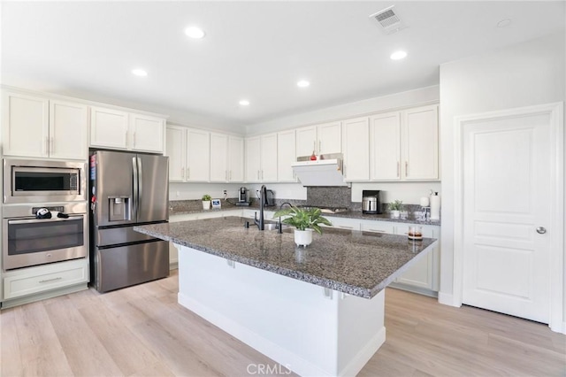 16138 Solitude Ave, Chino, CA 91708 - kitchen with stainless steel appliances, white cabinetry, light wood-type flooring, a kitchen island with sink, and dark stone countertops