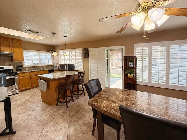 4474 Juanita Ct, Chino, CA 91710 - kitchen featuring stainless steel appliances, brown cabinetry, under cabinet range hood, a textured ceiling, and a ceiling fan