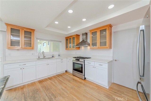 2406 Descanso Way, Torrance, CA 90504 - kitchen featuring wall chimney exhaust hood, stainless steel appliances, a tray ceiling, light wood-type flooring, and glass insert cabinets