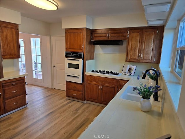 24921 Cypress St, Lomita, CA 90717 - kitchen featuring white appliances, a warming drawer, light wood-style floors, under cabinet range hood, and tile countertops