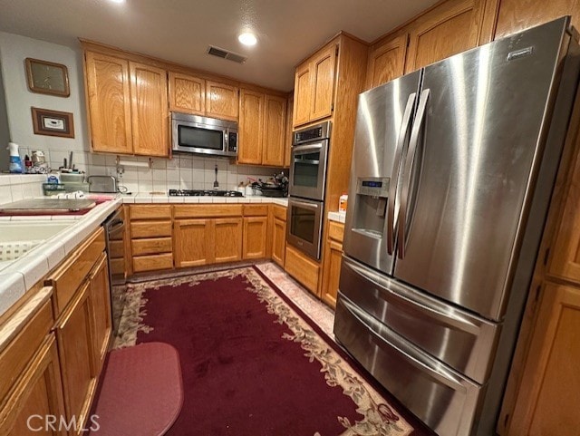 3854 Canvasback Ct, Merced, CA 95340 - kitchen with stainless steel appliances, tile countertops, decorative backsplash, recessed lighting, and brown cabinets
