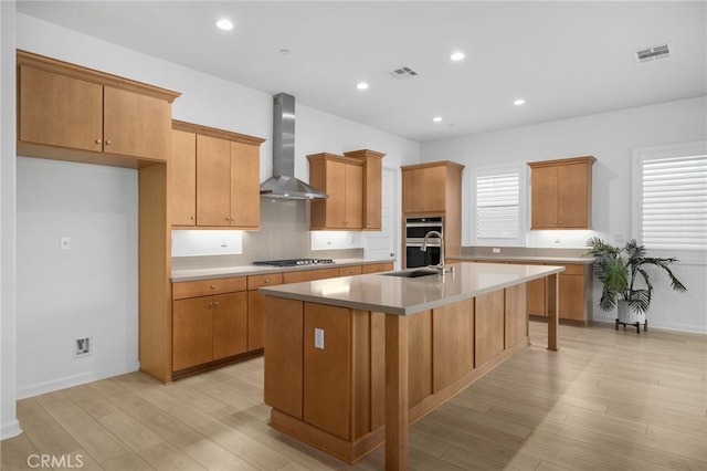 11937 Wandering Way, Corona, CA 92883 - kitchen with wall chimney exhaust hood, a kitchen island with sink, light wood-style floors, appliances with stainless steel finishes, and light countertops