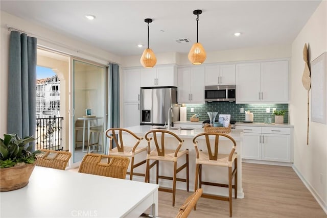 12247 Elliott Ave Unit C, El Monte, CA 91732 - kitchen with appliances with stainless steel finishes, tasteful backsplash, white cabinets, hanging light fixtures, and a kitchen island with sink