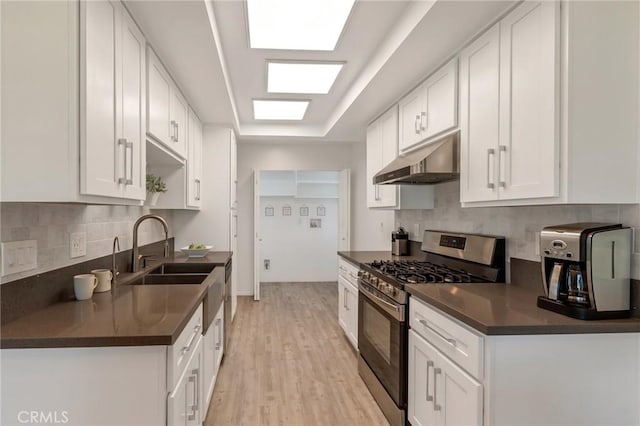 3246 Little Mountain Dr Unit D, San Bernardino, CA 92405 - kitchen with gas stove, dark countertops, under cabinet range hood, light wood-style flooring, and white cabinets