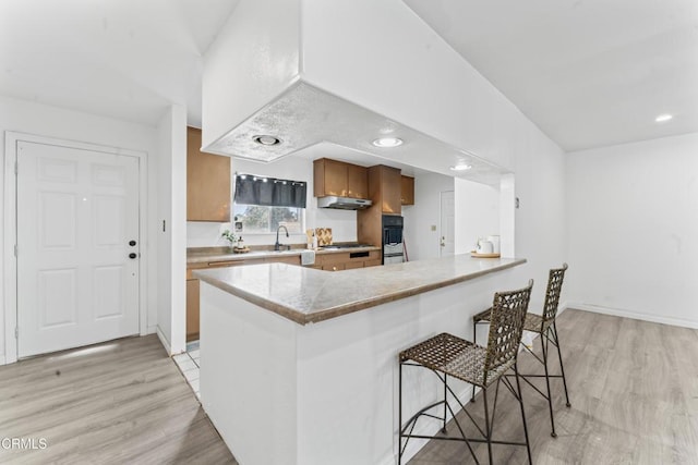 1904 N 7th St, Port Hueneme, CA 93041 - kitchen featuring under cabinet range hood, brown cabinets, a breakfast bar area, double oven, and light wood finished floors