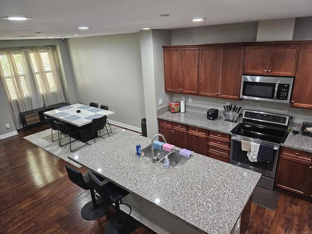 7508 Eagle Dr, Santee, CA 92071 - kitchen featuring appliances with stainless steel finishes, dark wood-style floors, a breakfast bar area, light stone counters, and a center island with sink