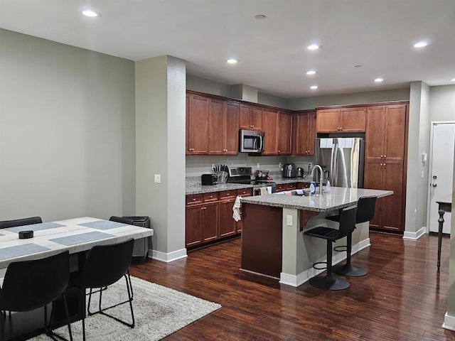 7508 Eagle Dr, Santee, CA 92071 - kitchen featuring appliances with stainless steel finishes, dark wood-style floors, a center island with sink, light stone counters, and a breakfast bar