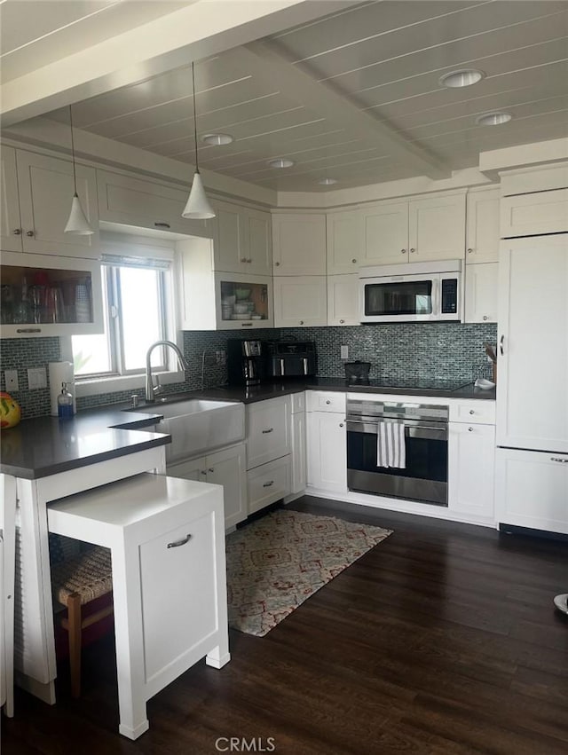 711 Pacific Coast Unit 109, Huntington Beach, CA 92648 - kitchen with stainless steel oven, white microwave, white cabinetry, dark countertops, and beamed ceiling