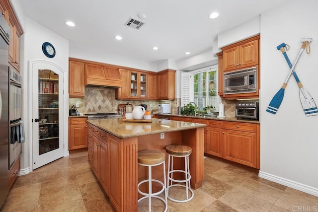 3239 Avenida La Cima, Carlsbad, CA 92009 - kitchen with stainless steel microwave, a center island, light stone countertops, decorative backsplash, and brown cabinets