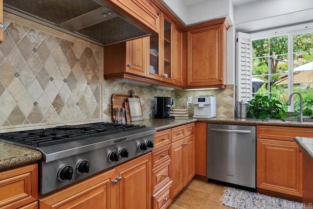 3239 Avenida La Cima, Carlsbad, CA 92009 - kitchen with appliances with stainless steel finishes, ventilation hood, brown cabinetry, glass insert cabinets, and backsplash
