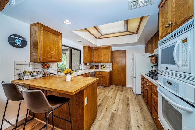 2278 Casitas Del Sol, Fallbrook, CA 92028 - kitchen featuring white appliances, a peninsula, a tray ceiling, brown cabinets, and light wood-style floors