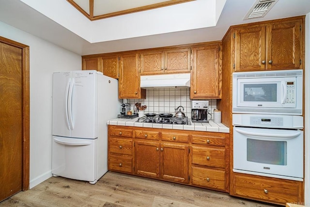 2278 Casitas Del Sol, Fallbrook, CA 92028 - kitchen with white appliances, under cabinet range hood, brown cabinetry, light wood-type flooring, and backsplash