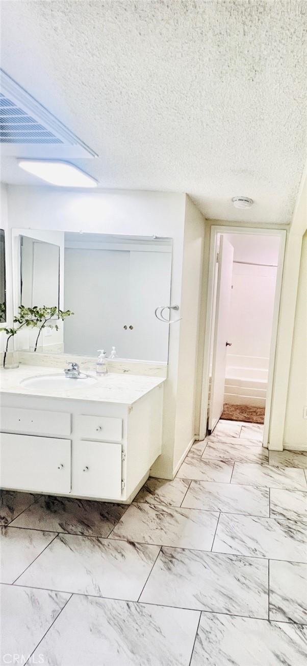 23515 Lyons Ave Unit 232, Valencia, CA 91355 - bathroom with vanity, a textured ceiling, marble look tile flooring, and a tub to relax in