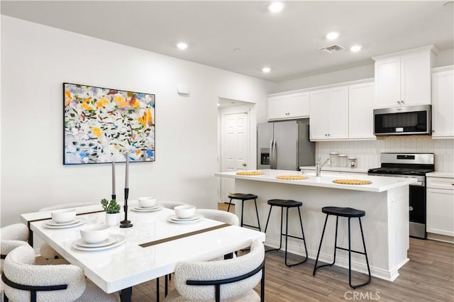 3957 E Huntington St, Ontario, CA 91761 - kitchen featuring stainless steel appliances, an island with sink, decorative backsplash, a kitchen bar, and white cabinetry