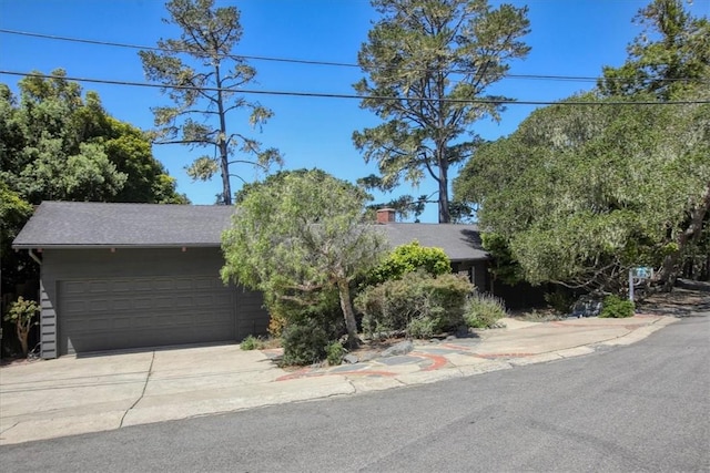2103 Benson Ave, Cambria, CA 93428 - view of property hidden behind natural elements with an attached garage, concrete driveway, a chimney, and a shingled roof