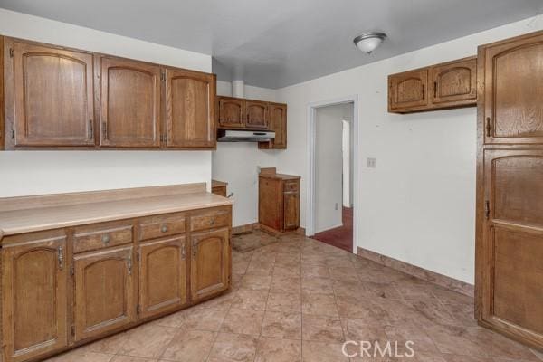 3014 E 3rd St, Los Angeles, CA 90033 - kitchen with brown cabinetry, under cabinet range hood, and light countertops