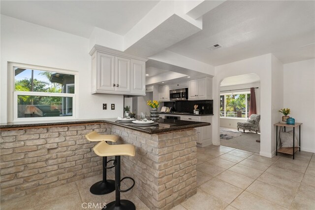 2041 Caballeros Rd, Norco, CA 92860 - kitchen with stainless steel microwave, a peninsula, white cabinetry, light tile patterned floors, and a breakfast bar