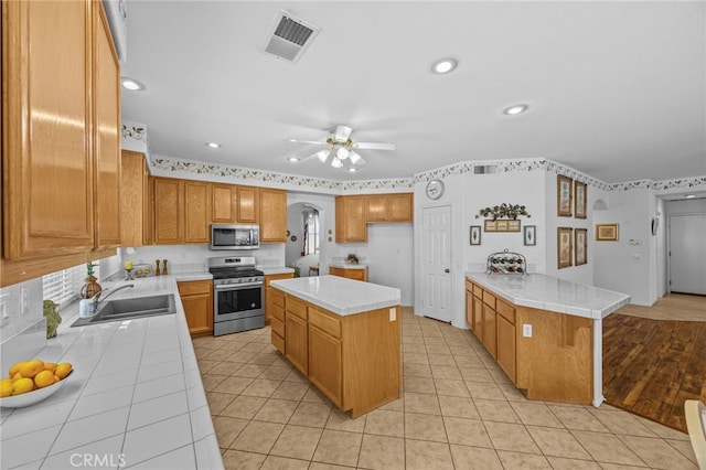 20865 Westbury Rd, Riverside, CA 92508 - kitchen featuring appliances with stainless steel finishes, tile countertops, arched walkways, light tile patterned flooring, and ceiling fan