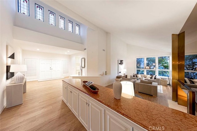 11 Montpellier Unit 22, Newport Beach, CA 92660 - kitchen featuring open floor plan, high vaulted ceiling, light wood finished floors, white cabinets, and light stone countertops