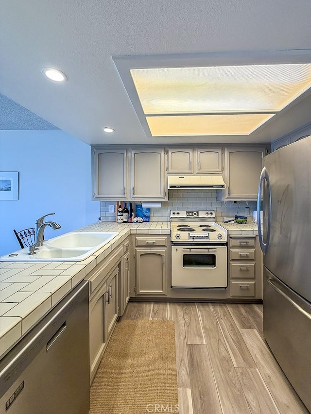 557 Lucerne St, Cayucos, CA 93430 - kitchen featuring stainless steel appliances, tile counters, under cabinet range hood, light wood-type flooring, and gray cabinets