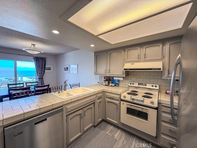 557 Lucerne St, Cayucos, CA 93430 - kitchen featuring appliances with stainless steel finishes, extractor fan, a peninsula, tile countertops, and gray cabinetry