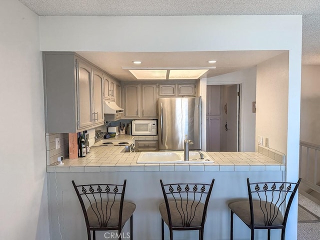 557 Lucerne St, Cayucos, CA 93430 - kitchen featuring white appliances, under cabinet range hood, a peninsula, tile counters, and a textured ceiling