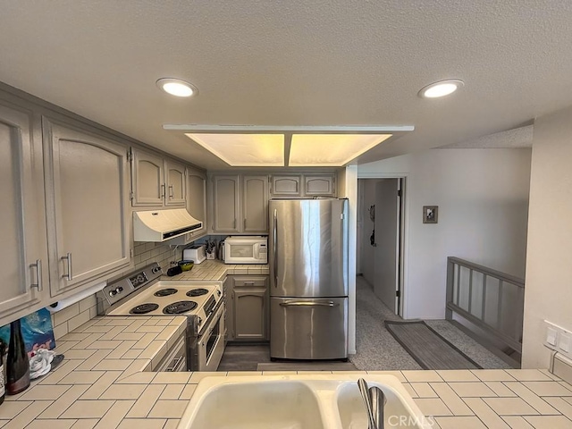 557 Lucerne St, Cayucos, CA 93430 - kitchen with tile countertops, freestanding refrigerator, electric range, under cabinet range hood, and white microwave