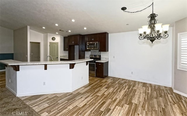 12745 Autumn Leaves Ave, Victorville, CA 92395 - kitchen featuring appliances with stainless steel finishes, light wood-type flooring, light countertops, a kitchen breakfast bar, and dark brown cabinets