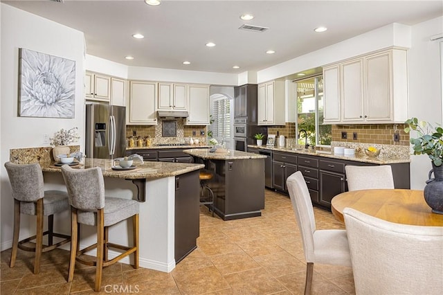 42355 Mountain View Ct, Murrieta, CA 92562 - kitchen with appliances with stainless steel finishes, under cabinet range hood, light stone countertops, a breakfast bar area, and decorative backsplash