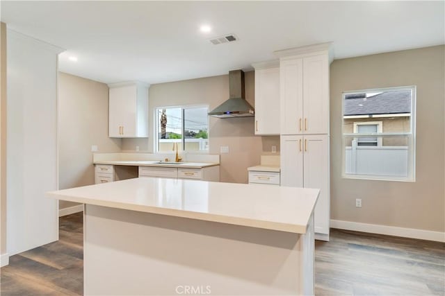 3067 Genevieve St, San Bernardino, CA 92405 - kitchen with wall chimney exhaust hood, dark wood finished floors, white cabinetry, a center island, and light countertops