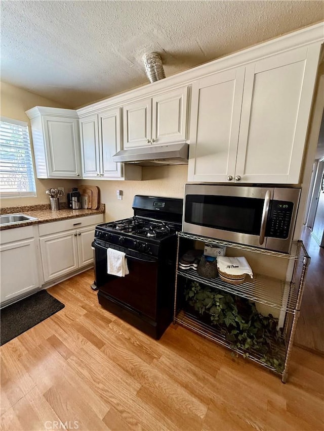 2616 N King St, Bakersfield, CA 93305 - kitchen with black gas stove, stainless steel microwave, under cabinet range hood, white cabinets, and light wood-type flooring