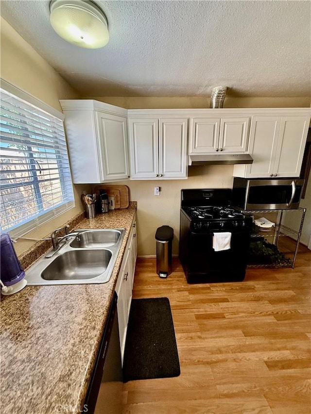 2616 N King St, Bakersfield, CA 93305 - kitchen with black gas range oven, stainless steel microwave, under cabinet range hood, light wood finished floors, and white cabinets