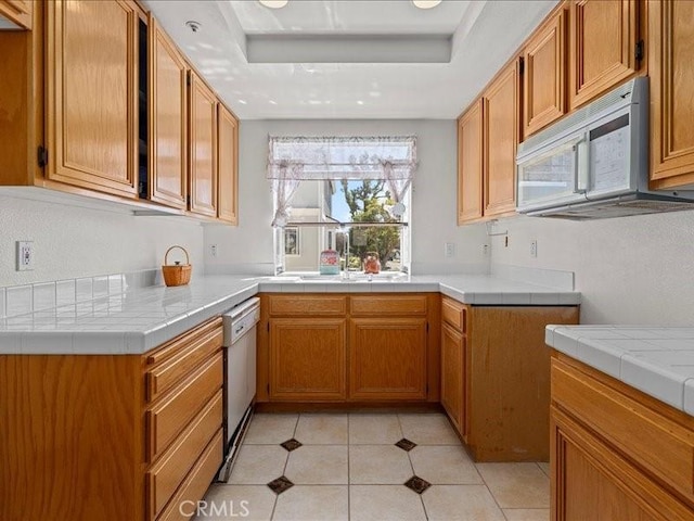 19025 Windridge Ln, Huntington Beach, CA 92646 - kitchen featuring white microwave, a raised ceiling, dishwashing machine, brown cabinetry, and light tile patterned floors