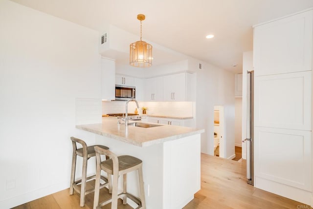 231 5th St, Encinitas, CA 92024 - kitchen featuring stainless steel microwave, light countertops, light wood finished floors, a breakfast bar area, and white cabinetry