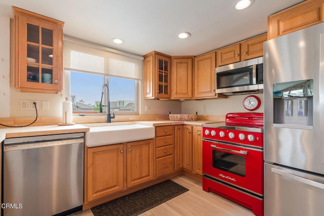 4534 La Brea St, Oxnard, CA 93035 - kitchen featuring appliances with stainless steel finishes, light countertops, light wood finished floors, brown cabinetry, and glass insert cabinets