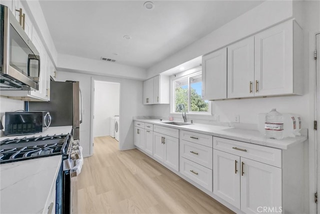18295 Aguiro St, Rowland Heights, CA 91748 - kitchen featuring stainless steel appliances, white cabinetry, washer and dryer, light stone counters, and light wood-type flooring