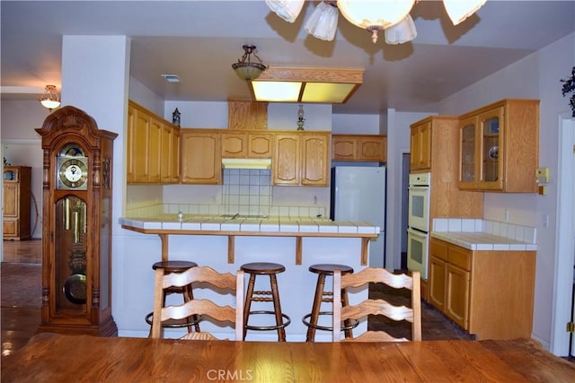 21509 Stage Dr, Tehachapi, CA 93561 - kitchen with tile counters, freestanding refrigerator, double oven, glass insert cabinets, and a peninsula