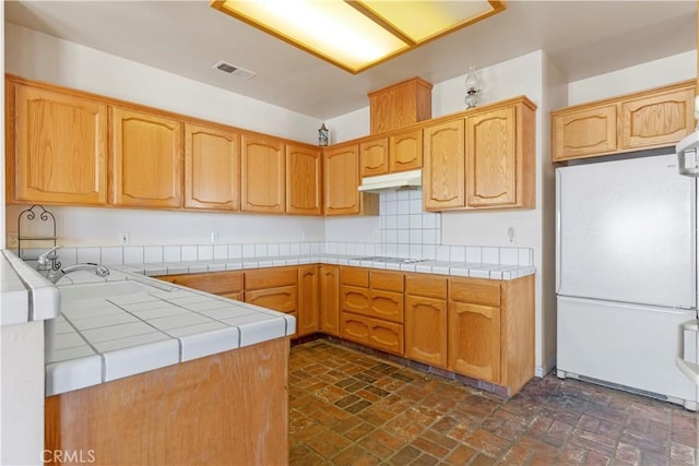 21509 Stage Dr, Tehachapi, CA 93561 - kitchen with freestanding refrigerator, under cabinet range hood, brick floors, and tile countertops